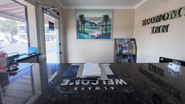 A reception desk with a 'Welcome' sign, a painting of a landscape, and a bookshelf with magazines. - ECONOMY INN (Santa Maria)