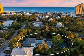 An aerial view of a coastal residential area with houses, a swimming pool, and tennis courts.