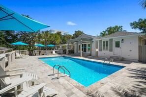 A swimming pool with clear blue water, surrounded by white lounge chairs and blue umbrellas.