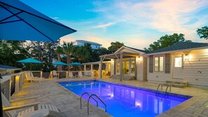 Ein Swimmingpool mit überdachter Terrasse, Liegestühlen und Sonnenschirmen.