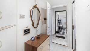A hallway with a wooden dresser, a mirror, a 'NO SMOKING' sign, and a door leading to a room with a checkered floor. - Ardenza's Aires 600m From Sea (Livorno)