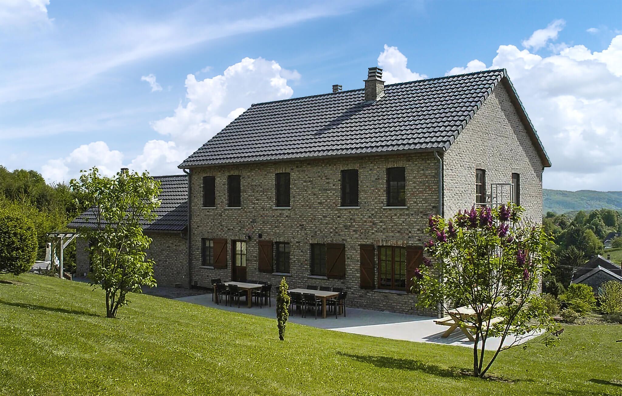 A stone house with a sloped roof, a patio with outdoor furniture, and a grassy lawn.
