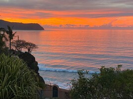 A coastal sunset view with rocky cliffs and vegetation.