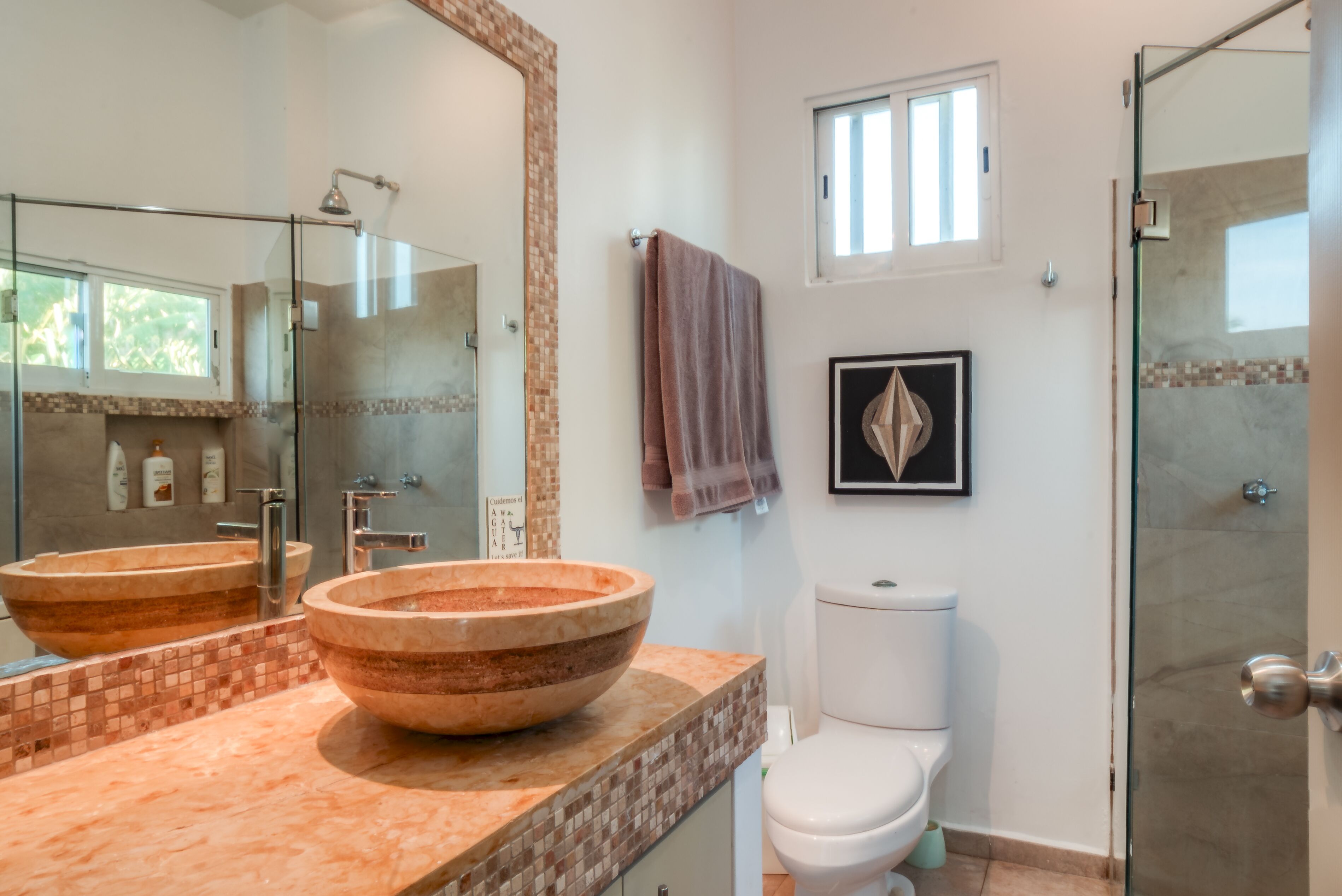 Une salle de bain avec deux grands lavabos ronds en bois, des toilettes blanches, une douche en verre et une petite fenêtre.