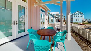 A covered patio with a wooden table and turquoise chairs, overlooking a beach with houses in the background. - Resort Pools, Pet Friendly, Golf Cart Boardwalk to Beach (Port Aransas)