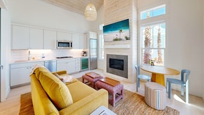A modern kitchen with white cabinets, a microwave, and a built-in oven. There is a fireplace with a painting above it and a dining area with a table and chairs. - Resort Pools, Pet Friendly, Golf Cart Boardwalk to Beach (Port Aransas)