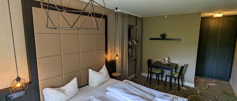 A hotel room with a large bed, a desk with chairs, a small table with a vase of flowers, and a wardrobe.