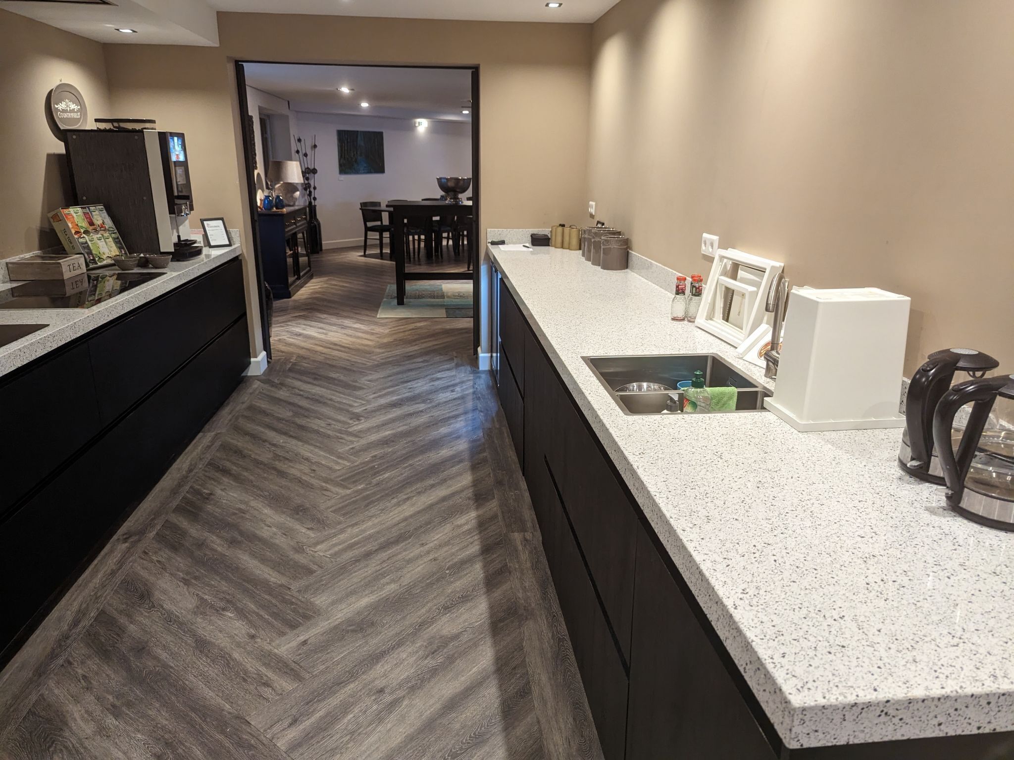 A modern kitchen with a herringbone floor, a large island with a sink, and a dining area in the background.