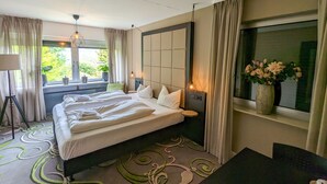 A hotel room with a large bed, a desk, a chair, a window with curtains, a lamp, and a vase with flowers. - Gruppe Meisenberg by Interhome (Winterberg)