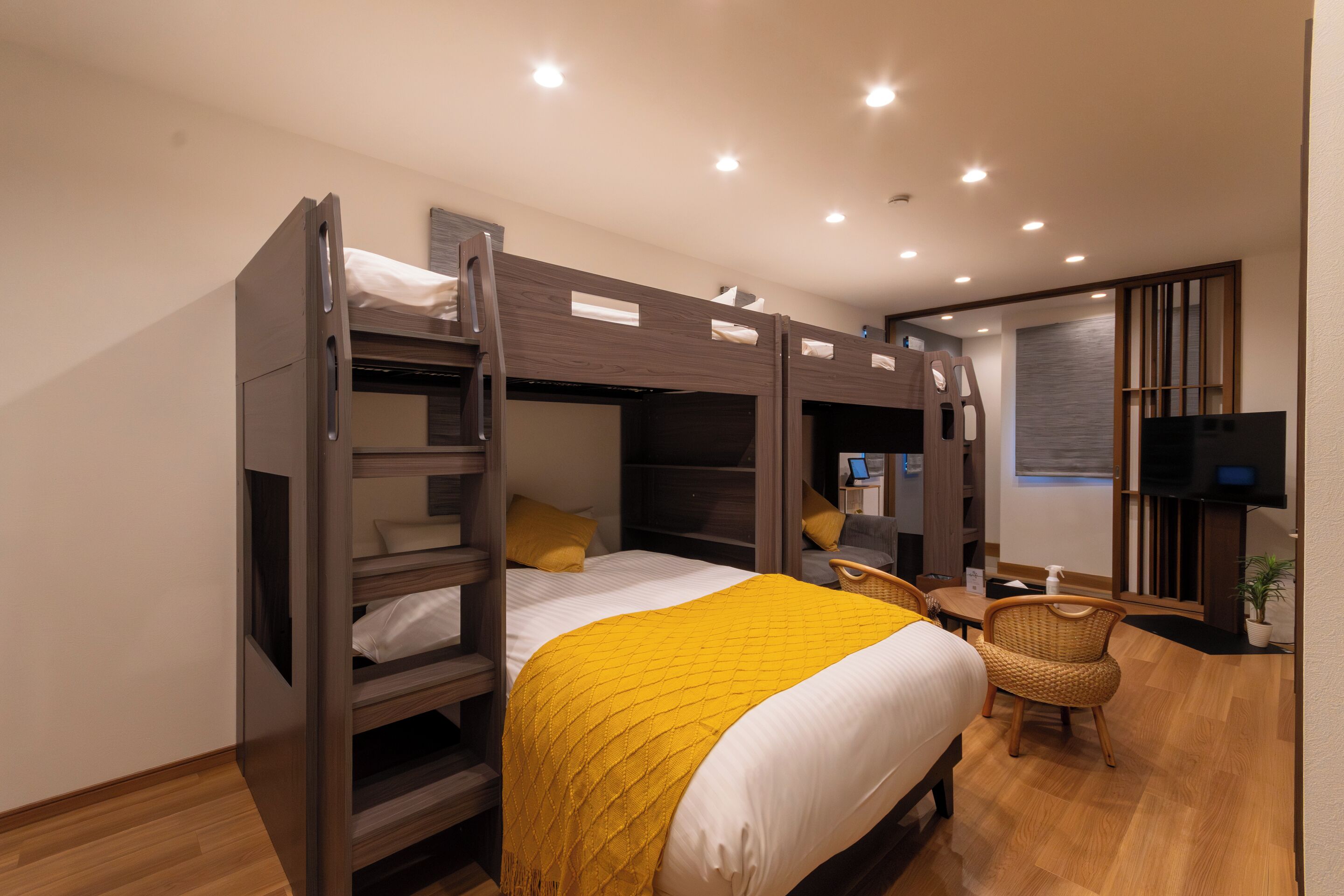 A bunk bed room with a yellow blanket, a desk, a chair, and a TV.
