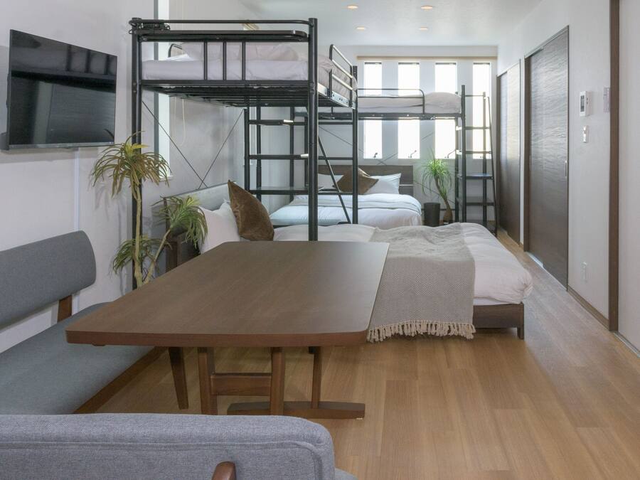 Quarto moderno e compacto com beliches, uma mesa de jantar de madeira e uma televisão fixada na parede.
