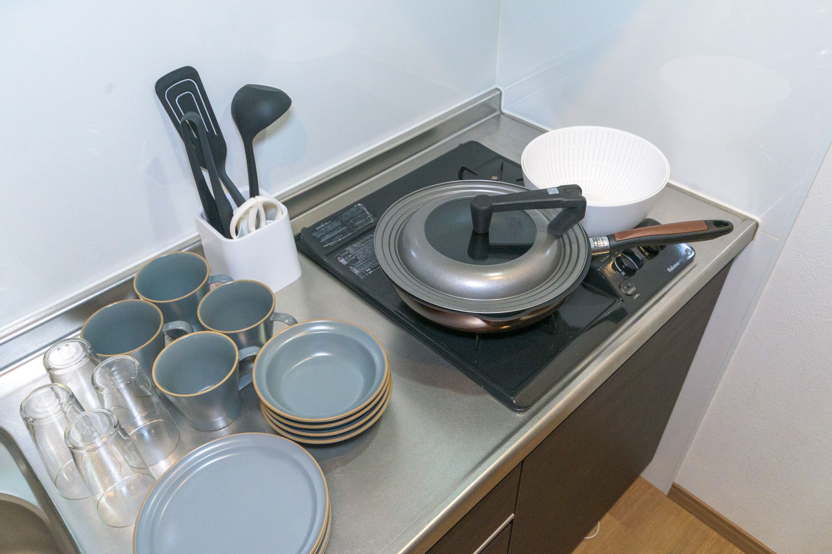 A kitchen counter with a stove, a white bowl, a stack of plates, and a container holding utensils.