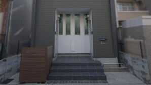 Un bâtiment moderne à deux étages, avec une façade grise, une porte blanche et un petit escalier menant à l’entrée.