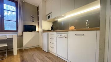A compact kitchen with white cabinets, a wooden countertop, a built-in microwave, and a dishwasher.