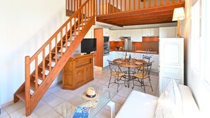 A spacious living area with a wooden staircase, a dining table with chairs, and a kitchen in the background. - Le Green Village by Interhome (Roquebrune sur Argens)
