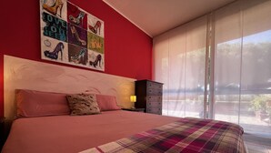 Un dormitori amb un llit, una petita taula de nit, un armari i una finestra amb persianes, i un quadre amb bótes al mur.