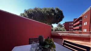 Un edifici vermell amb una taula, cadires, un cactus i un gran arbre al fons.