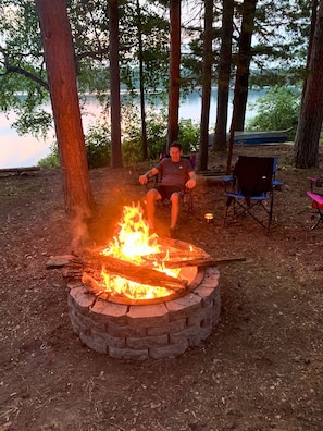 A person relaxing by a campfire in a forested area with a lake in the background. - Ford's Talpine Cottage on Echo Lake (Mercer)
