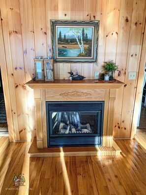 A wooden-paneled room with a fireplace, a framed painting above it, and decorative items on the mantel. - Ford's Talpine Cottage on Echo Lake (Mercer)