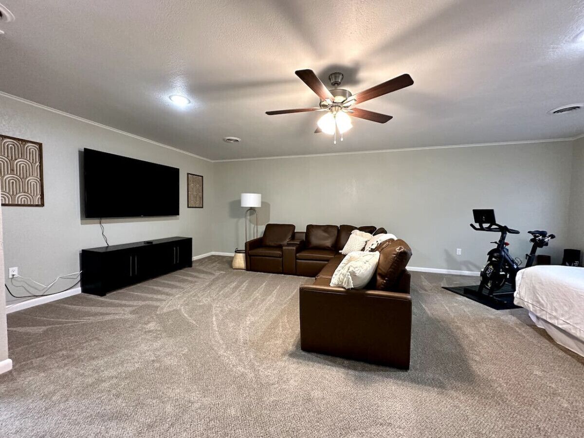 A spacious living room with a large flat-screen TV, a ceiling fan, a sofa, a coffee table, and a stationary bike.