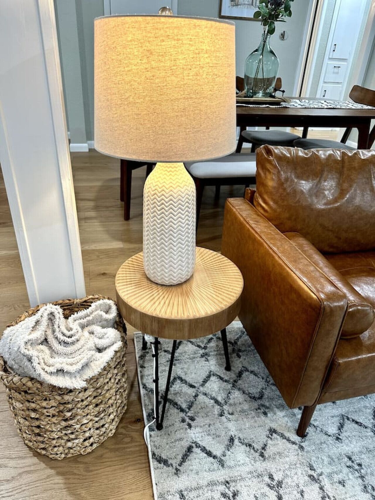 A modern living room with a wooden side table, a brown leather sofa, a woven basket, and a patterned rug.