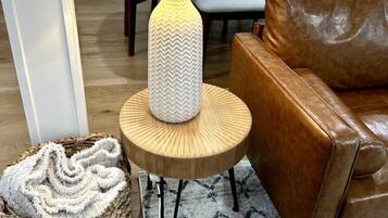 A modern living room with a wooden side table, a brown leather sofa, a woven basket, and a patterned rug.