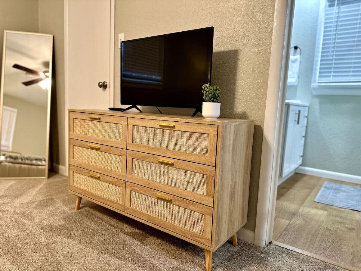 Une commode en bois avec des tiroirs, un téléviseur posé dessus et une petite plante en pot.