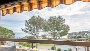 Una mesa con una botella de jugo, un bol de fruta y un plato en un balcón con vistas a la costa, árboles y un estacionamiento.