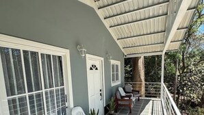 Eine überdachte Veranda mit Fliesenboden, weißen Stühlen und einer Tür mit Fenster.