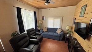 Ein Wohnzimmer mit einer Couch, einem Ledersessel, einem an der Wand befestigten Fernseher und einem Deckenventilator.