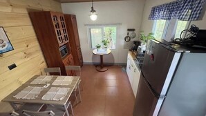 Eine kleine Küche mit Esstisch, Stühlen, einem Kühlschrank und einem Fenster mit Vorhängen.