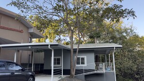 Ein modernes Haus mit überdachter Veranda, einem davor geparkten Auto und einem Baum in der Nähe.