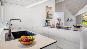 Et moderne køkken med hvide skabe, en sort bordplade og en skål med grøntsager på bordet.