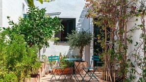 A courtyard with a white building, a table, two chairs, and potted plants. - Lovely studio in peaceful courtyard (Arroyo De La Miel)