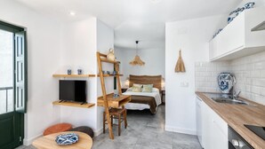 A compact hotel room with a kitchenette, a bed with a woven headboard, a TV mounted on the wall, and a small wooden table. - Lovely studio in peaceful courtyard (Arroyo De La Miel)