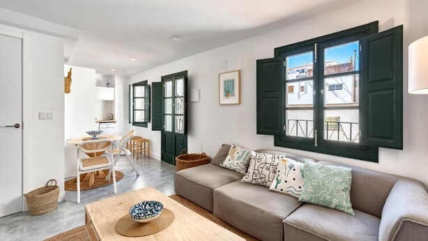 A modern living room with a sofa, a dining table, and a kitchen area in the background. - Lovely studio in peaceful courtyard (Arroyo De La Miel)