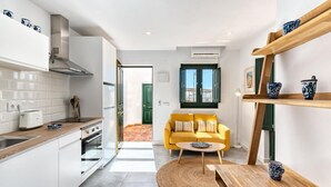 A modern kitchen with white cabinets, a yellow sofa, and a wooden dining table. - Lovely studio in peaceful courtyard (Arroyo De La Miel)