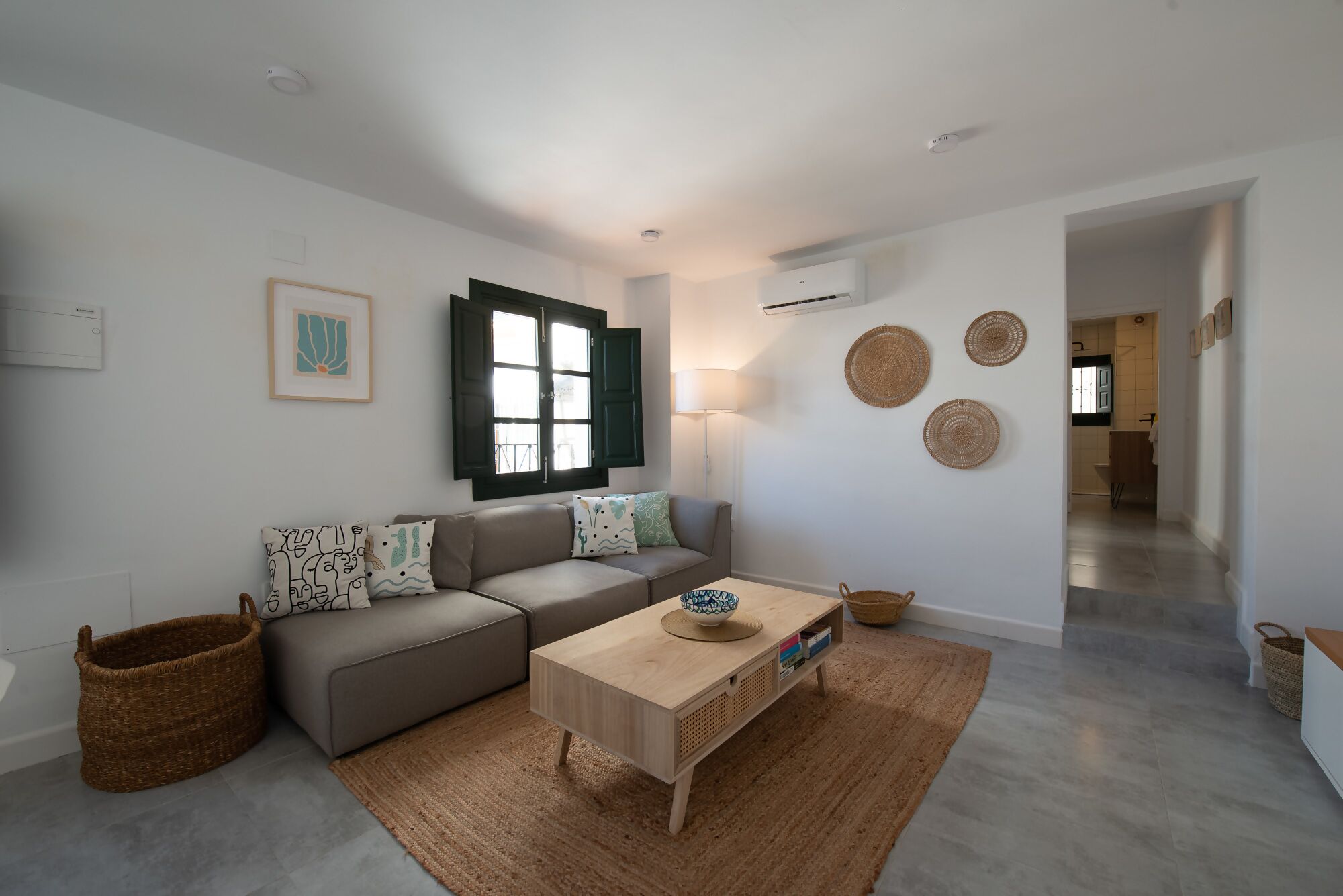 A modern living room with a sofa, a coffee table, and a wall-mounted air conditioner.