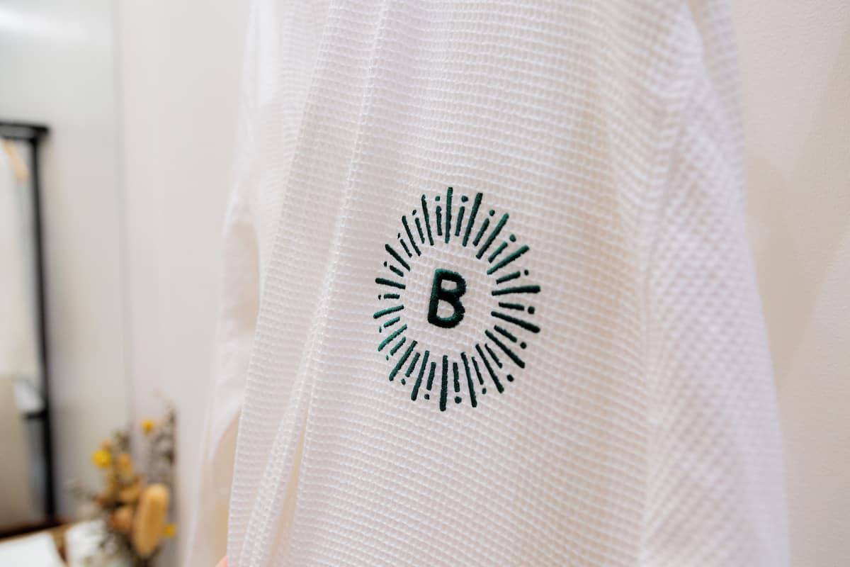 A close-up of a white textured fabric with a circular logo featuring a stylized 'B' and radiating lines.