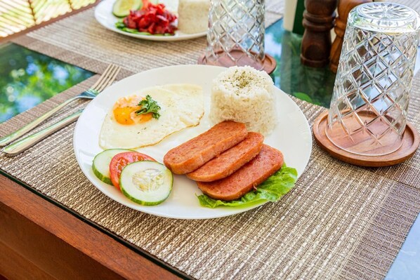 Un plato con huevos revueltos, arroz, lonchas de salchicha y rodajas de pepino sobre una mesa con un mantel tejido.