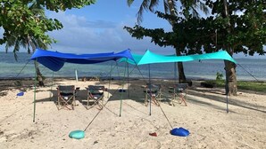A beach with two blue canopies providing shade, several beach chairs, and a clear view of the ocean. - Bahandi Hotel (General Luna)