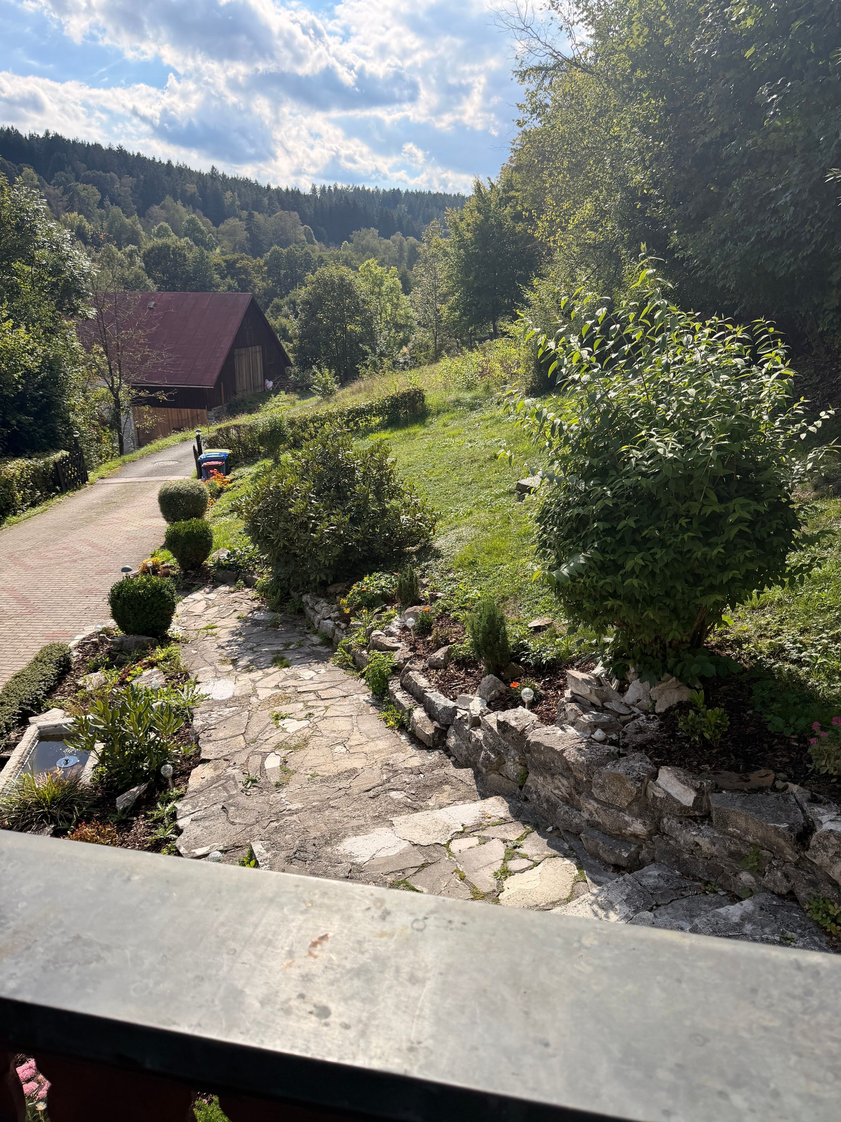 A rural road with a stone pathway, a wooden barn, and lush greenery.