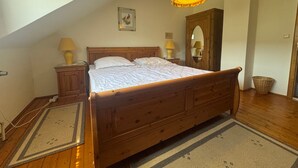 Une chambre à coucher avec un lit en bois, deux lampes de chevet, une suspension, un miroir et une armoire en bois.