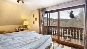 Une chambre à coucher comprenant un lit, une table de chevet, une lampe et donnant sur un balcon avec une balustrade.
