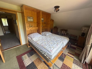 Una cama individual en una habitación con cabecera de madera, ventilador de techo y alfombra de retazos.