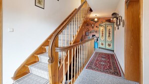 Un escalier en bois, recouvert d’une moquette à motifs, mène à une pièce dont un mur est en briques et qui contient un meuble orné de panneaux décoratifs.