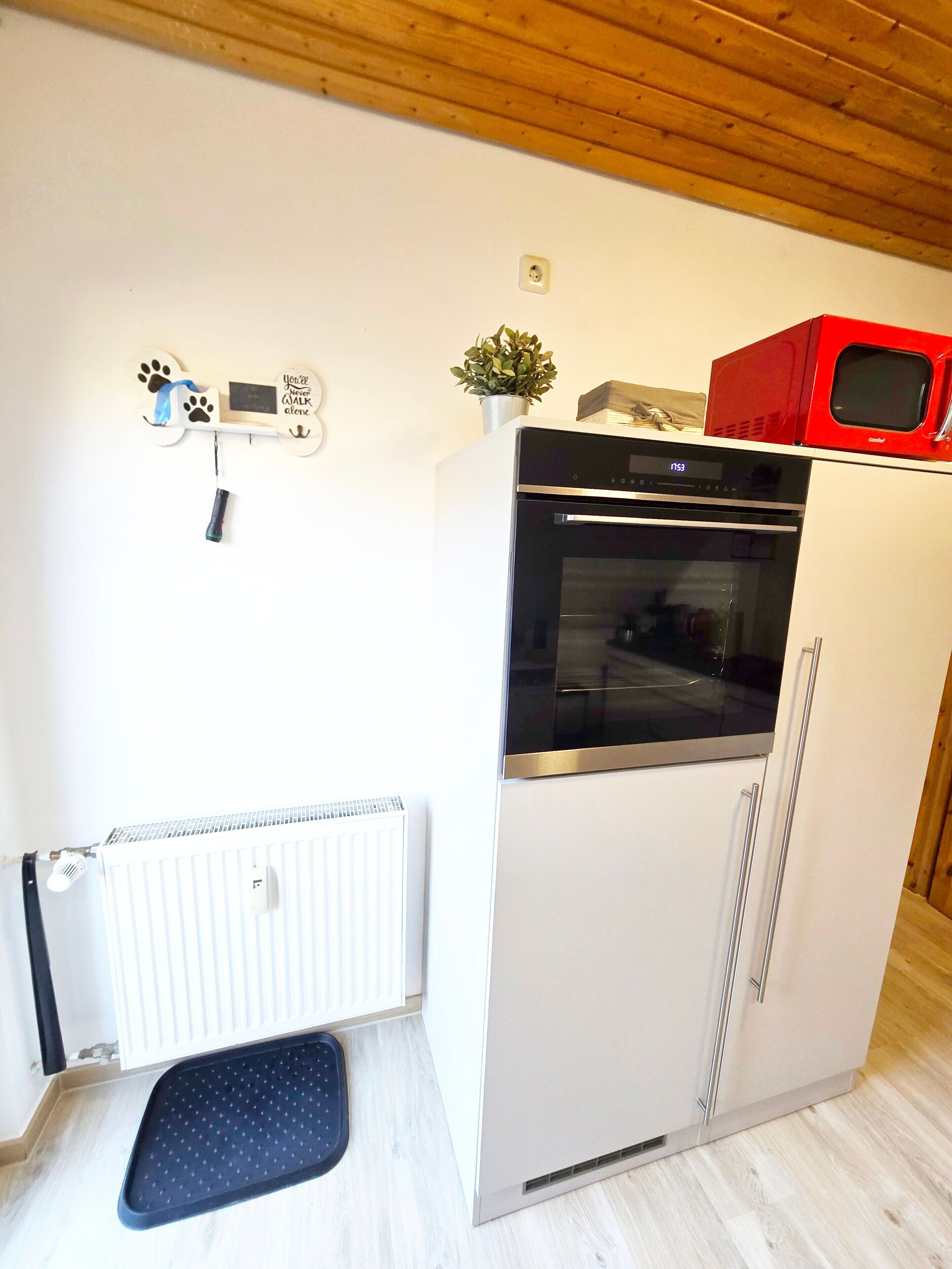 A compact kitchen with a built-in oven, a microwave, and a small potted plant on top.
