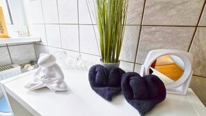 A bathroom with a white countertop, a white ceramic Buddha statue, a vase with green plants, and a white towel warmer with a folded towel. - Apartment Waldblick with Large Balcony, Ground-Level Access, and Unique Forest View (Bestwig)