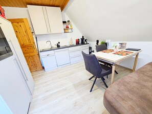 Una cocina moderna con armarios blancos, una puerta de madera y un comedor con mesa y sillas.