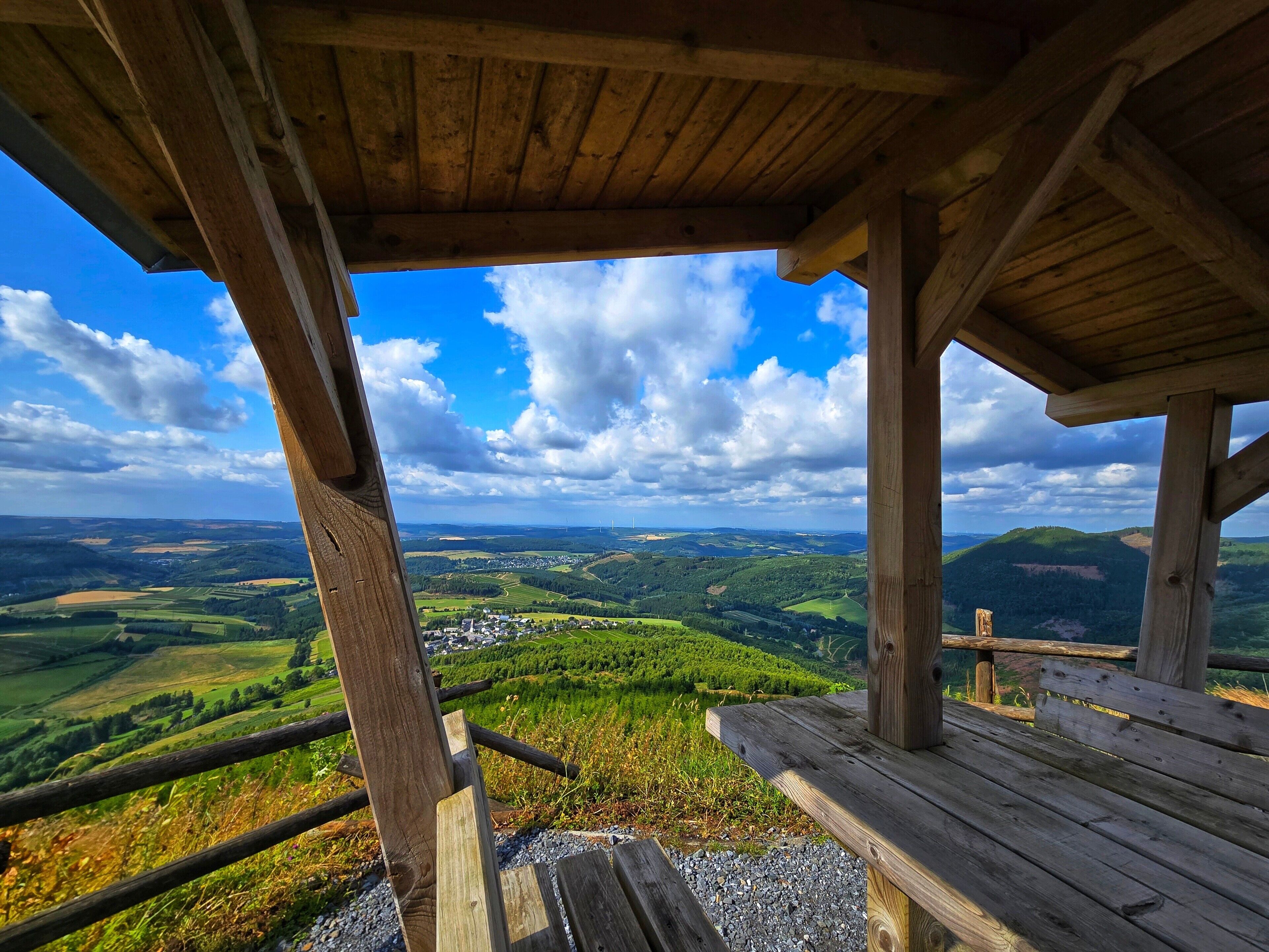 A wooden observation deck with a view of a valley and distant wind turbines.